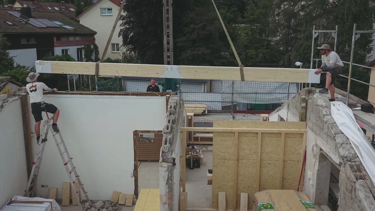 Die neue Firstpfette wird am Kran über den Bestandswänden eingesetzt