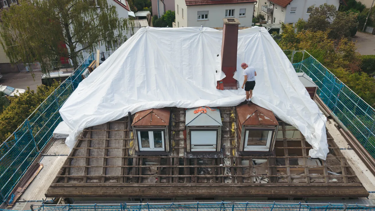 Teilweise geöffnetes Walmdach, dessen Dachflächen mit Schutzplanen gesichert sind